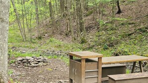 Un banc et une table en bois rustique, installés dans une zone boisée, avec un tas de pierres à proximité.