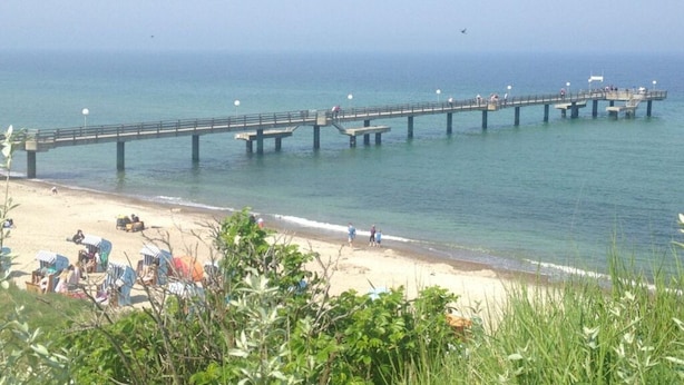 A pier extending into calm waters with a sandy beach in the foreground. - Albatros in the House of Aquarius (Rerik)
