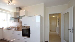 A modern kitchen with white cabinetry, a built-in oven, and a stainless steel range hood. - Albatros in the House of Aquarius (Rerik)