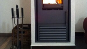 A modern fireplace with a glass front, a metal stand with candles, and a wicker basket nearby. - Albatros in the House of Aquarius (Rerik)