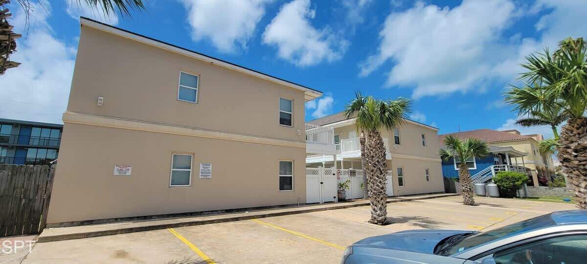 A two-story building with a flat facade, a gated entrance, and a parking area with palm trees.