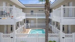 A two-story building with a pool, white railings, and potted plants. - In Entertainment District - Ample Bedding - Pool (South Padre Island)