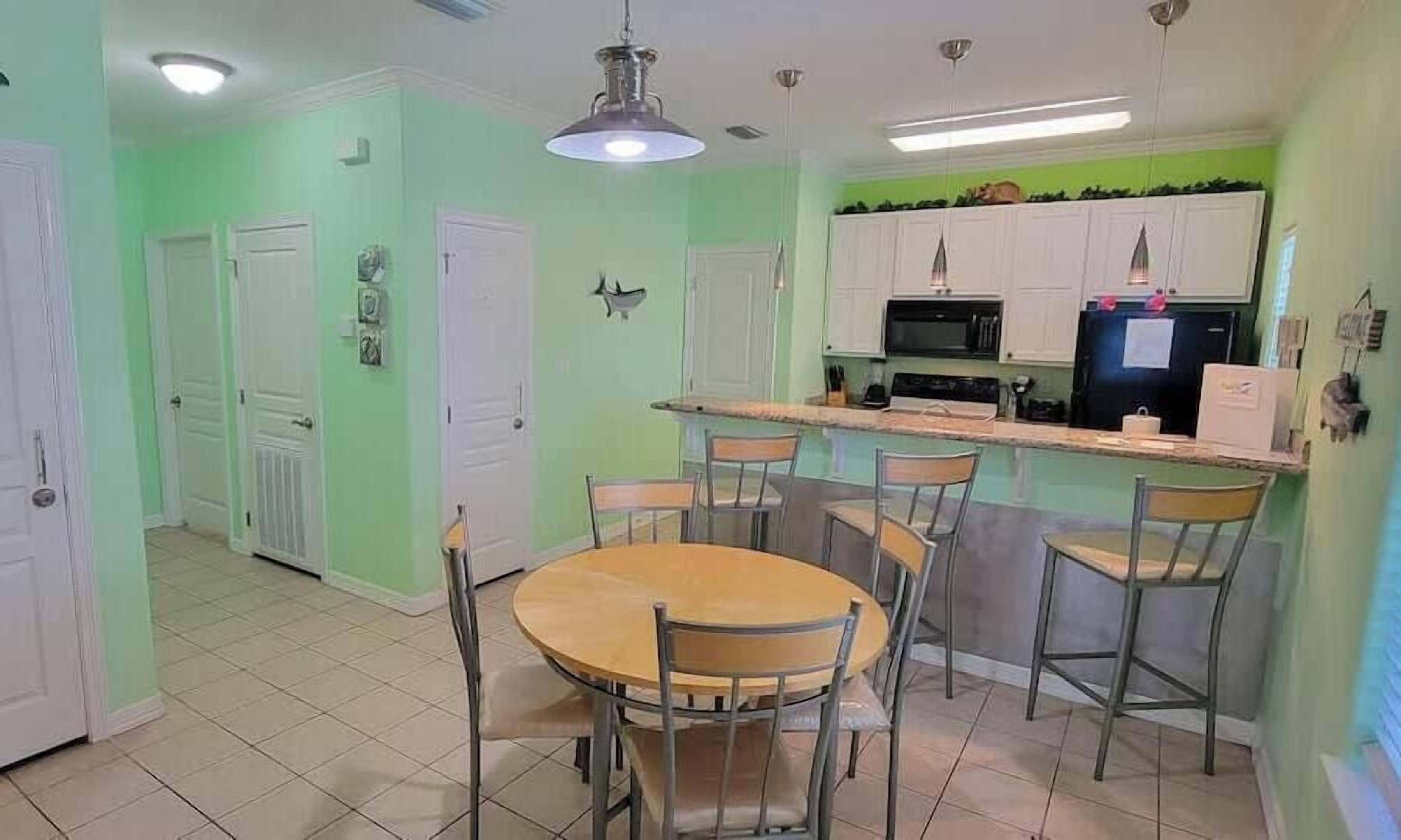 A compact kitchen with a dining area, featuring a central island with bar stools, white cabinets, and a microwave.