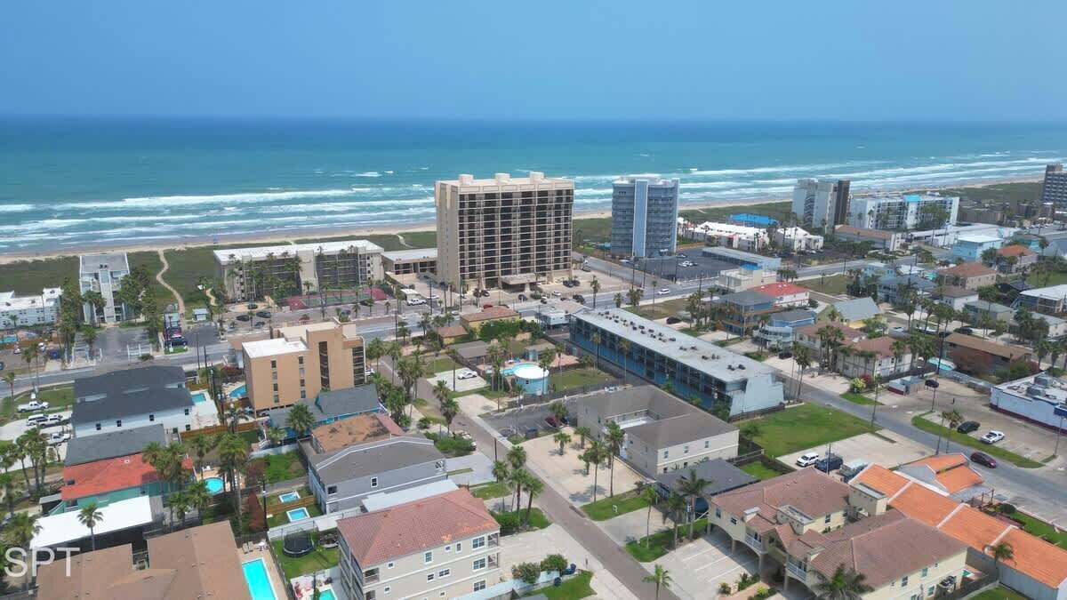 An aerial view of a coastal city with a prominent hotel building, a beach, and a clear view of the ocean.