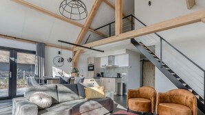 A modern living room with a sofa, armchairs, and a coffee table. A staircase leads to an upper level. - Beautiful House With air Conditioning (Baarle-Nassau)