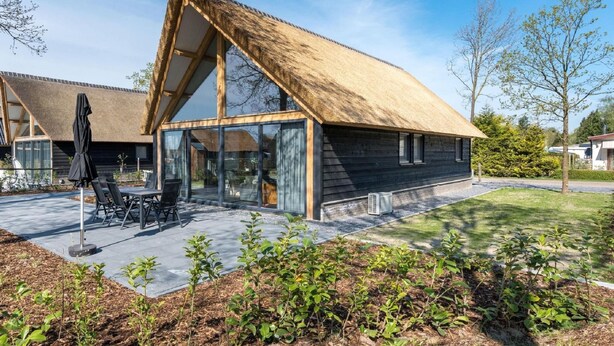 A modern house with a thatched roof, large windows, and a patio area with outdoor furniture. - Beautiful House With air Conditioning (Baarle-Nassau)