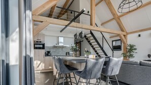 A modern kitchen with a central island, a dining area with chairs, and a staircase leading to an upper level. - Beautiful House With air Conditioning (Baarle-Nassau)