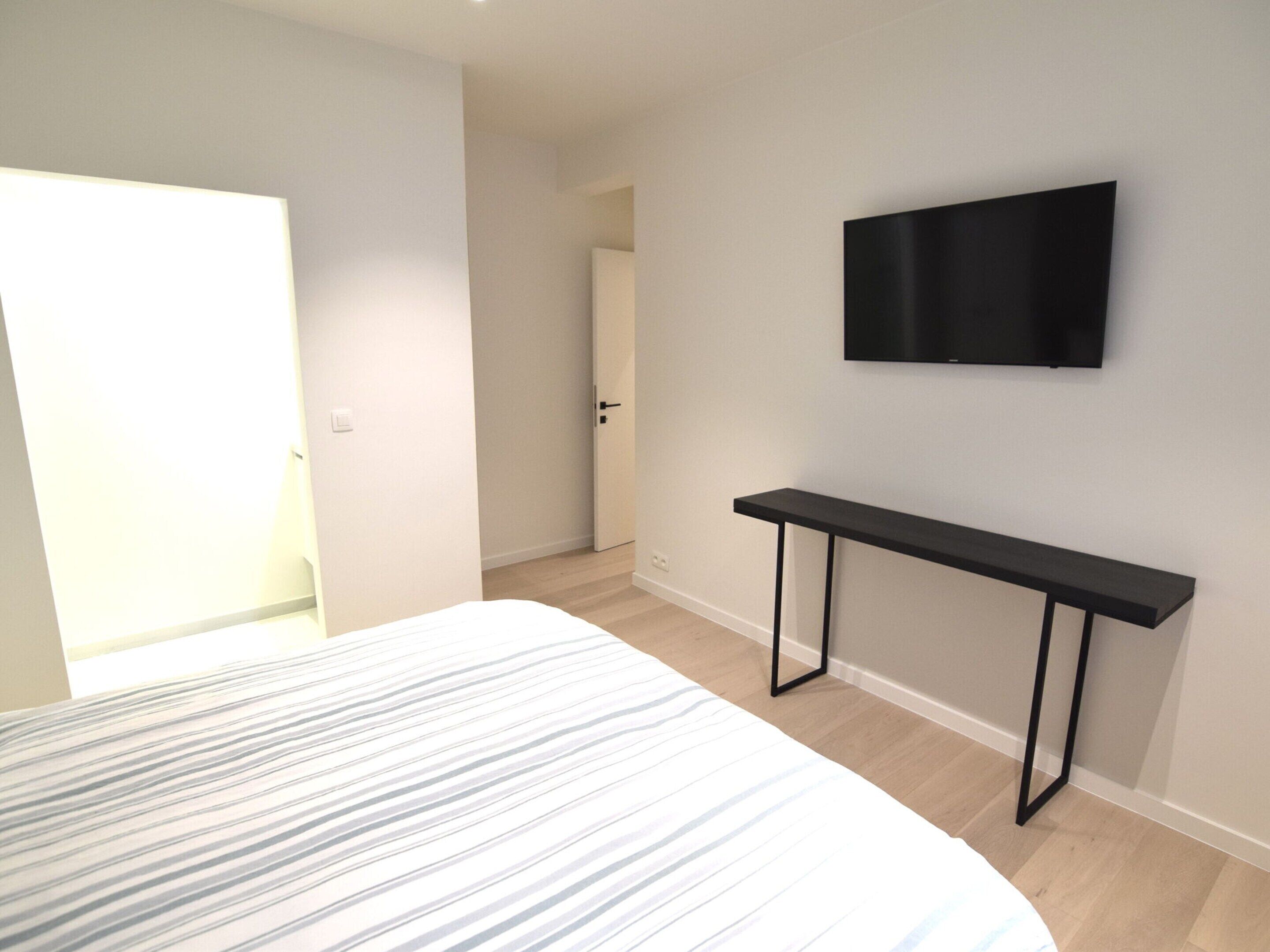 A bedroom with a bed, a TV mounted on the wall, and a door leading to another room.