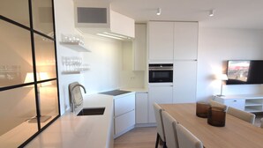 Eine moderne Küche mit weißen Schränken, einem eingebauten Backofen und einem Essbereich mit einem Holztisch und Stühlen.