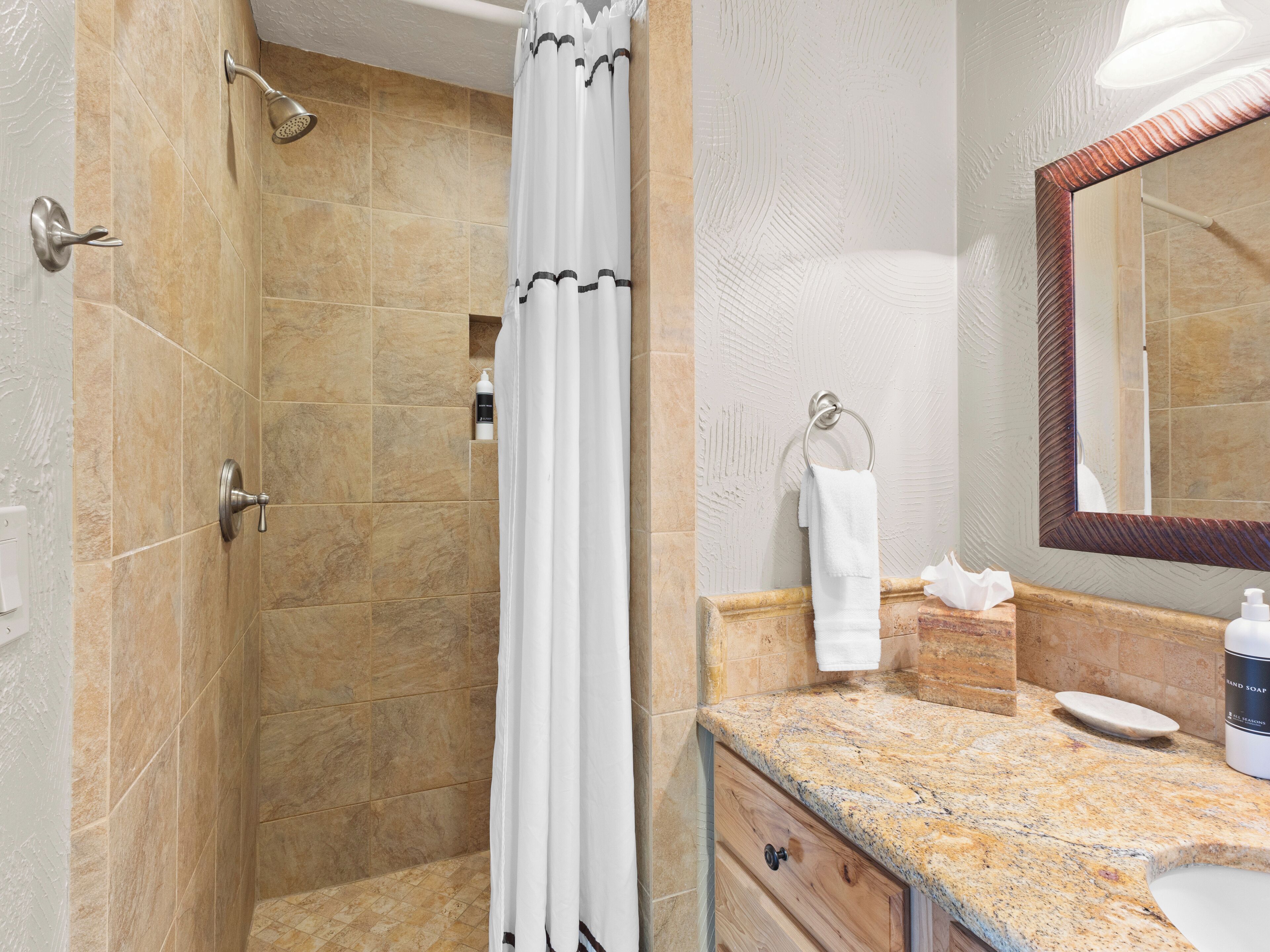 A bathroom with a shower, a sink, a mirror, and a towel rack.