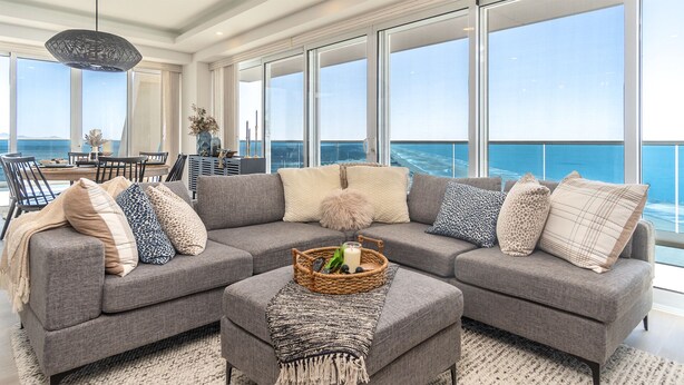 A modern living room with a gray sectional sofa, a coffee table with a candle and a basket, and a view of the ocean through large windows. - Wonderful 1 Bedroom condominium Encantame Verano 2103 (Puerto Peñasco)