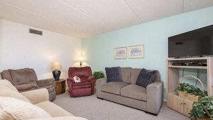 A living room with a sofa, armchair, and a television on a stand. - Padre Oasis #302 (South Padre Island)
