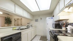 A compact kitchen with white cabinets, a dishwasher, a stove, and a microwave. - Padre Oasis #302 (South Padre Island)