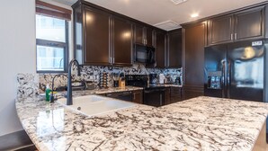 A modern kitchen with dark wood cabinets, a stainless steel refrigerator, a built-in microwave, and a granite countertop. - Las Palomas 3 BR 2 BA Topaz 801 (Puerto Peñasco)