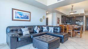 A modern living room with a sectional sofa, ottoman, and a dining area with wooden chairs and a table. - Las Palomas 3 BR 2 BA Topaz 801 (Puerto Peñasco)