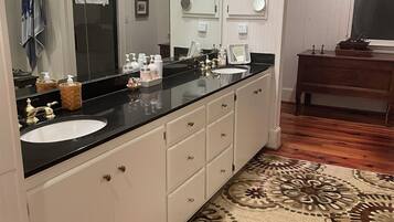 A bathroom with a large mirror, a black countertop, a white sink, and a wooden floor.