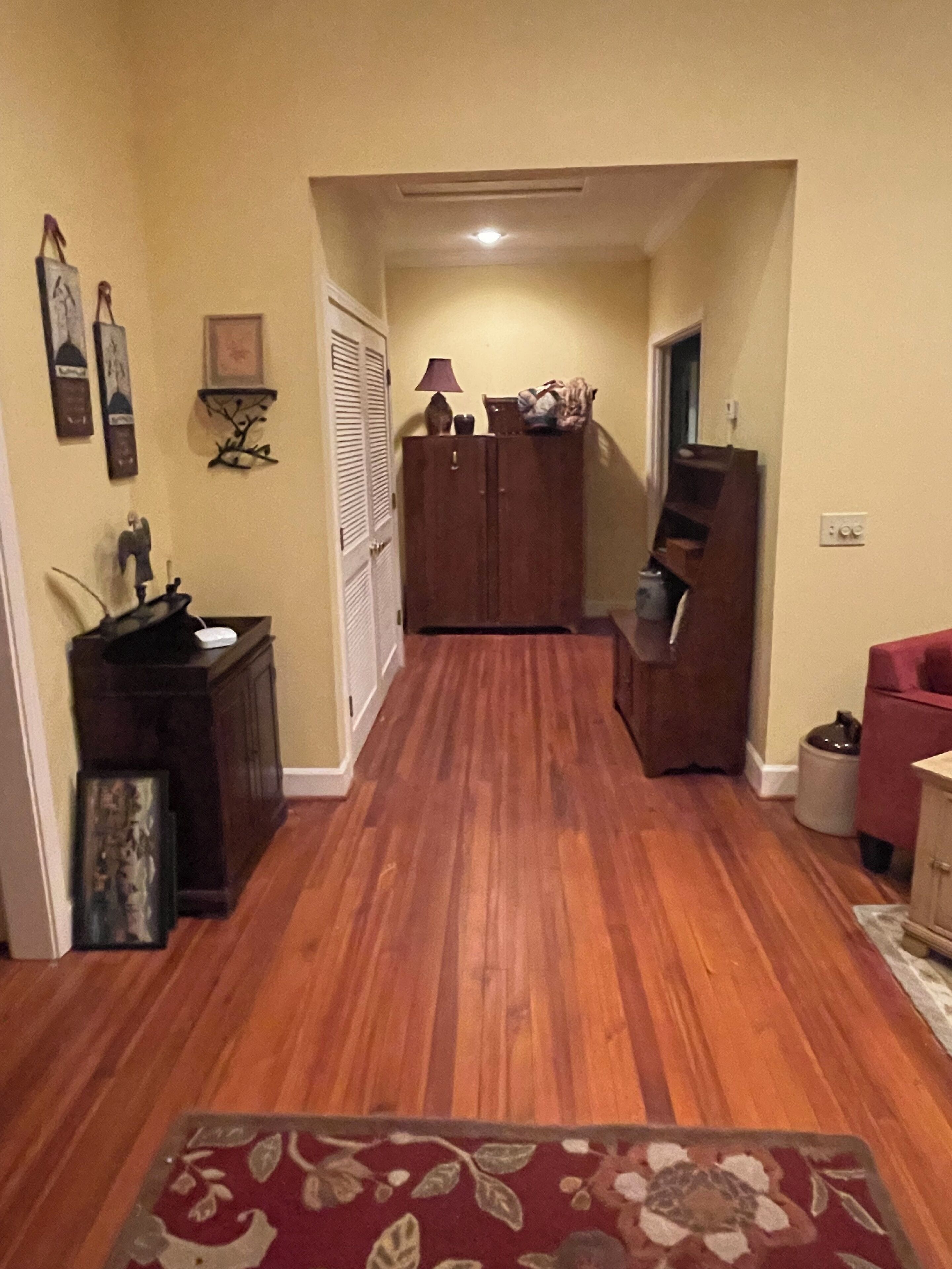 Un pasillo con suelo de madera, un tapete rojo, un armario y un piano.