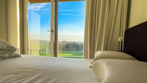 A hotel room with a large bed, a view of a green landscape through a glass door, and a dark headboard. - Apartment in Nieuwpoort Near the Beach (Nieuwpoort)