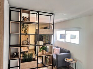 Ein modernes Wohnzimmer mit grauem Sofa, einem kleinen runden Tisch und einer eingebauten Holzregaleinrichtung mit verschiedenen dekorativen Objekten und Pflanzen.