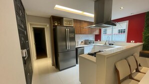 A modern kitchen with a central island, stainless steel appliances, and a red accent wall. - Casa de Luxo, com Piscina na Penha, ZL. Aceita day use até 30 Pessoas (Jardim Popular São Paulo)