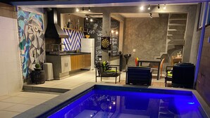 A swimming pool with blue lighting, a kitchen area with a chalkboard, and a dining area with chairs and tables. - Casa de Luxo, com Piscina na Penha, ZL. Aceita day use até 30 Pessoas (Jardim Popular São Paulo)