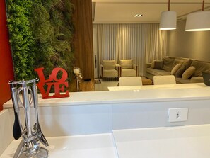 A modern living room with a white reception desk, a green wall with a 'LOVE' sign, and a sofa set. - Casa de Luxo, com Piscina na Penha, ZL. Aceita day use até 30 Pessoas (Jardim Popular São Paulo)