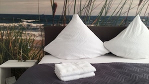 A bed with a dark quilt, two white pillows, and a folded white towel.