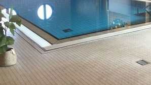 An indoor swimming pool with a tiled floor, a wooden ceiling, and a wall with circular windows.