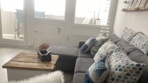 A living room with a grey sofa, patterned cushions, a wooden coffee table, and a fluffy white rug.