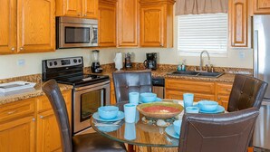 A kitchen with wooden cabinets, stainless steel appliances, a glass dining table with chairs, and a window with blinds. - 4 Bedroom 2 Level Home - 50 Yards From Beach (South Padre Island)