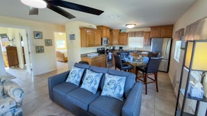 A modern kitchen with wooden cabinets, a dining area with a glass table, and a gray sofa with decorative pillows. - 4 Bedroom 2 Level Home - 50 Yards From Beach (South Padre Island)