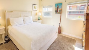 A bedroom with a bed, nightstands, a lamp, a vase, a window with blinds, and a wall-mounted cabinet. - 4 Bedroom 2 Level Home - 50 Yards From Beach (South Padre Island)