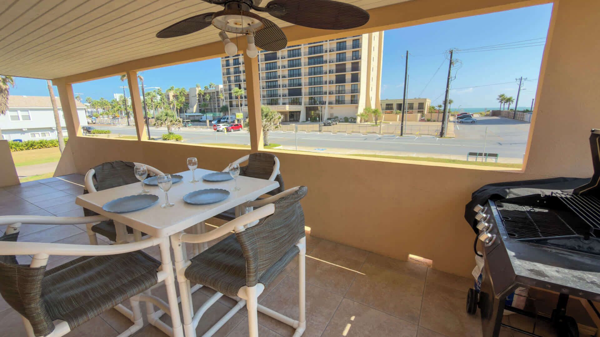 An outdoor patio with a table set for dining, a grill, and a view of a street and buildings.