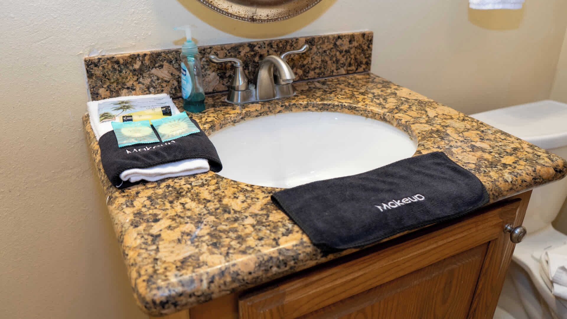 A bathroom with a granite countertop, a sink, a towel, and a bottle of hand soap.
