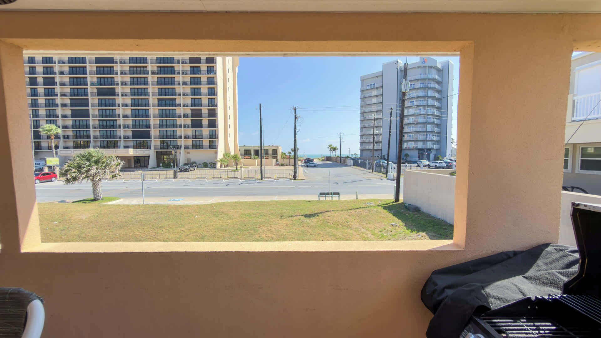 A view from a window overlooking a street with buildings, a parking lot, and a grassy area.