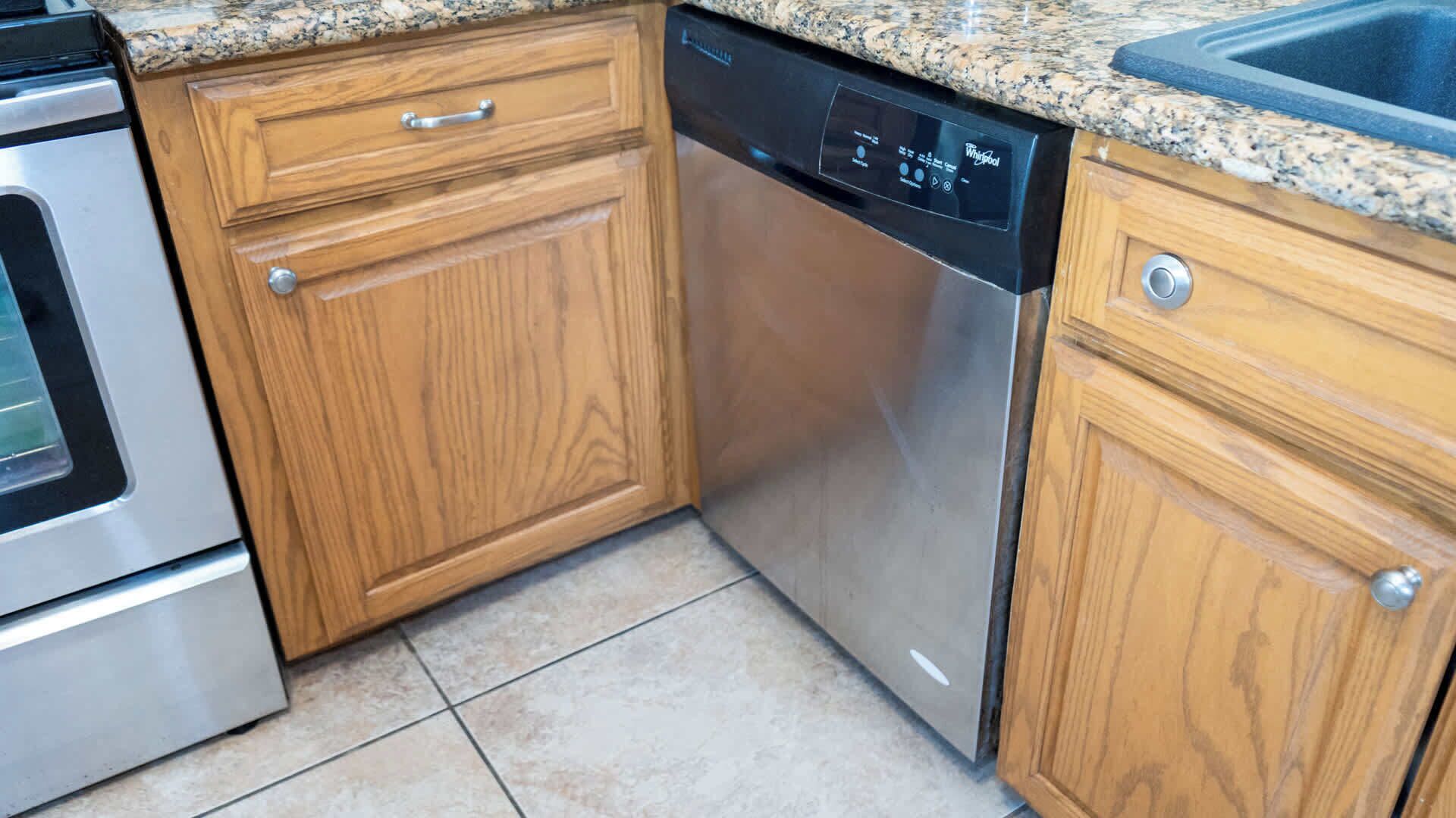 Una cocina con armarios de madera, lavavajillas de acero inoxidable y encimera de granito.