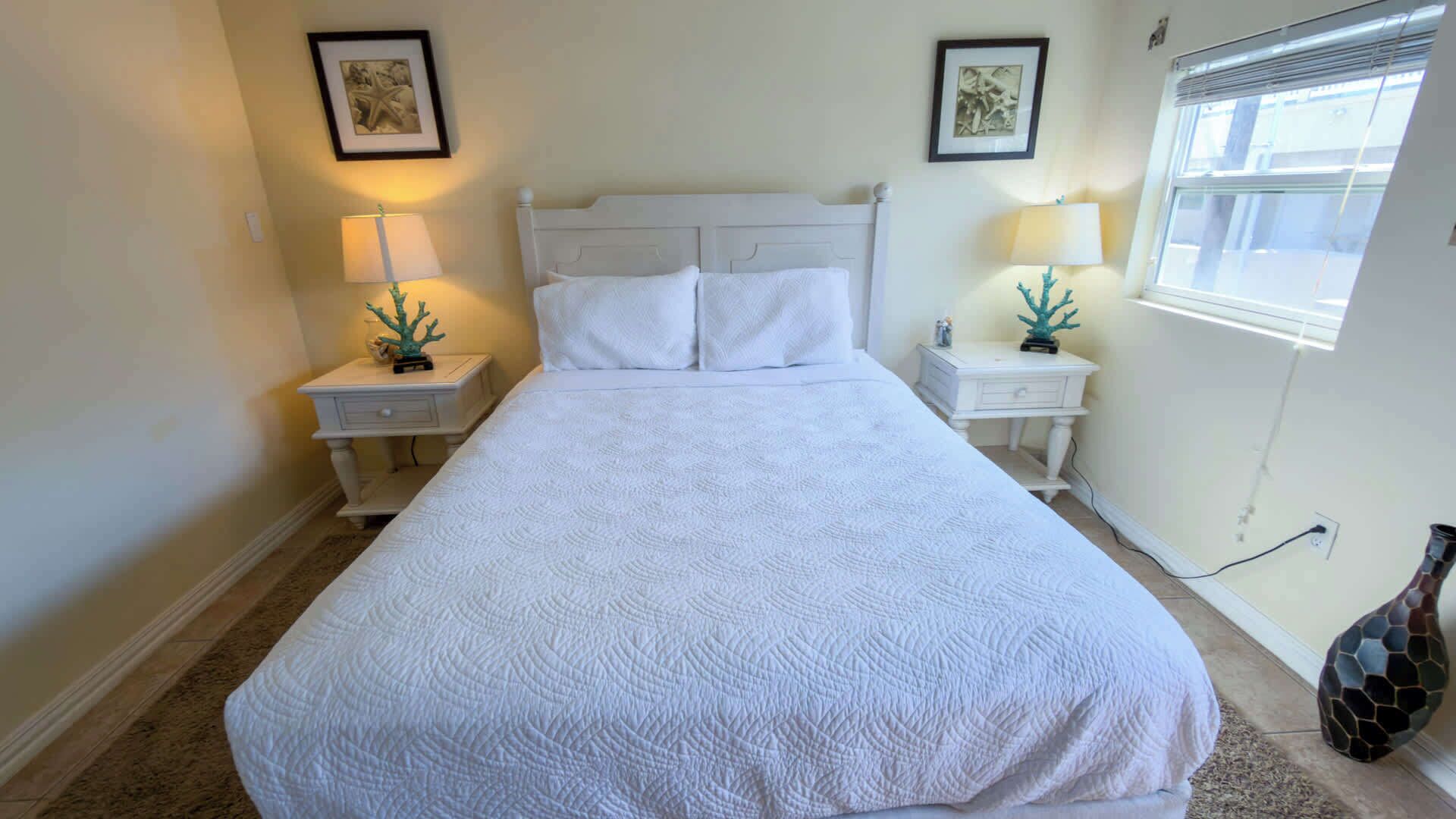 A neatly made bed with white bedding in a room with two bedside tables, each with a lamp and a small decorative item.