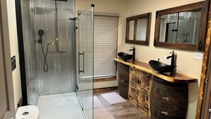 A bathroom with a glass shower enclosure, a toilet, a sink with a wooden vanity, and a mirror above the sink. - Come stay at the quite and Cozy 
Rustic Hideaway  (Edwards)