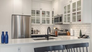 A modern kitchen with white cabinetry, stainless steel appliances, and a central island with seating.