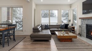 A modern living room with a sectional sofa, a dining table with chairs, and a fireplace.