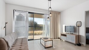 Uma sala de estar moderna com sofá, TV, mesa de centro e porta de vidro deslizante que dá para uma varanda.
