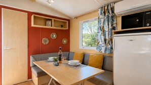 A compact kitchenette with a refrigerator, a microwave, and a window with curtains. - Le Romarin, mobile home with sea view (Hyères)