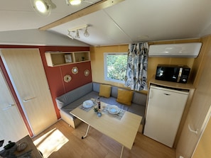Enjoy a compact living space with a sofa, dining table, kitchenette, and window view of the surrounding greenery.