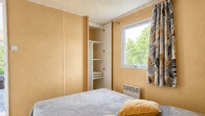 A bedroom with a bed, two pillows, a window with curtains, and a wardrobe. - Le Romarin, mobile home with sea view (Hyères)
