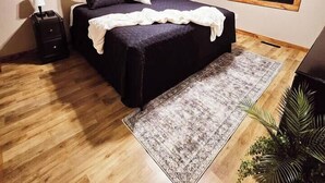 Une chambre à coucher comprenant un lit, un ventilateur de plafond, une table de chevet, une lampe, un tapis et un cadre photo fixé au mur.