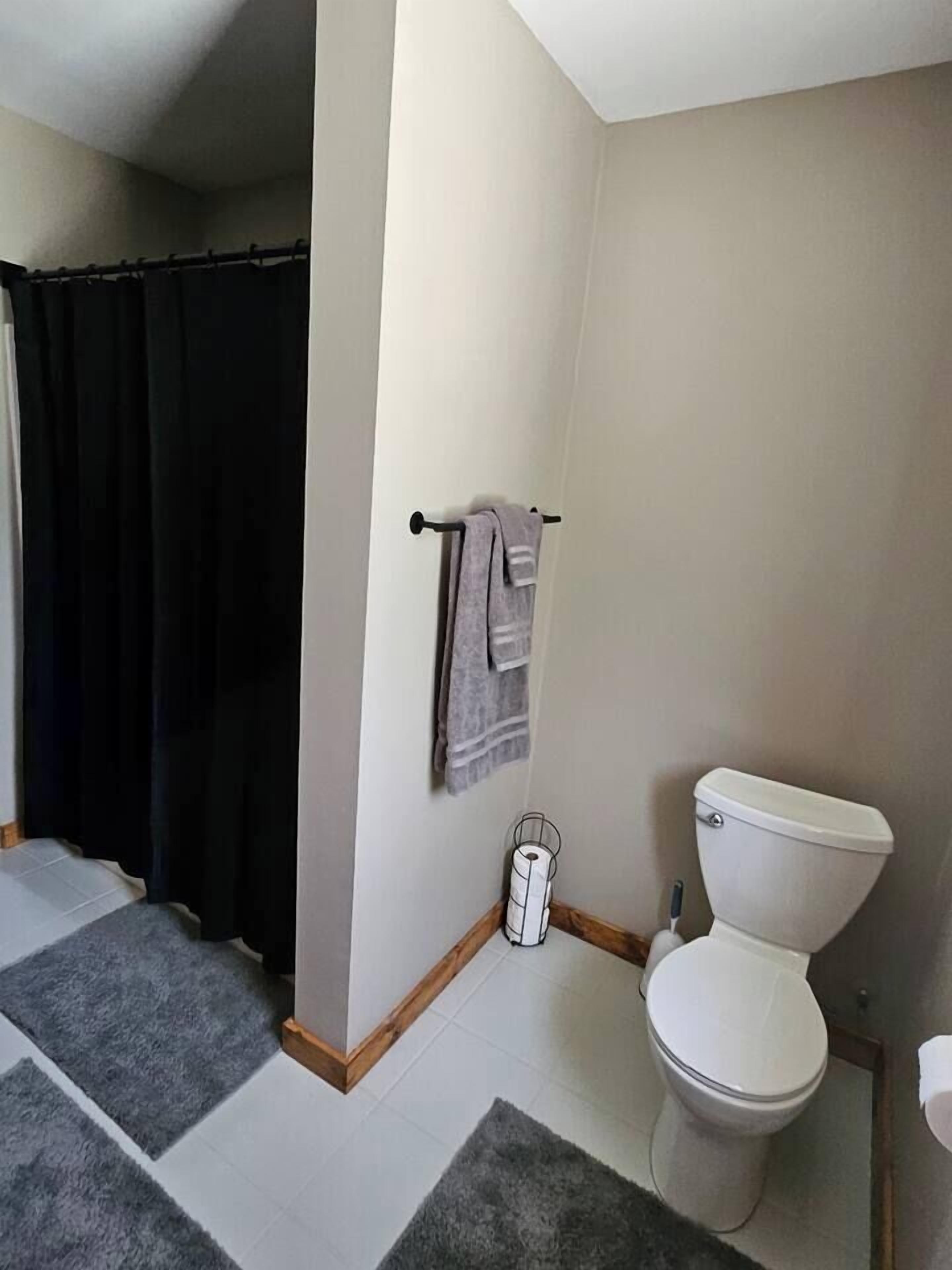 Ein Badezimmer mit Toilette, Handtuchhalter mit Handtüchern, einer Duschvorhang und einer Toilettenbürste.
