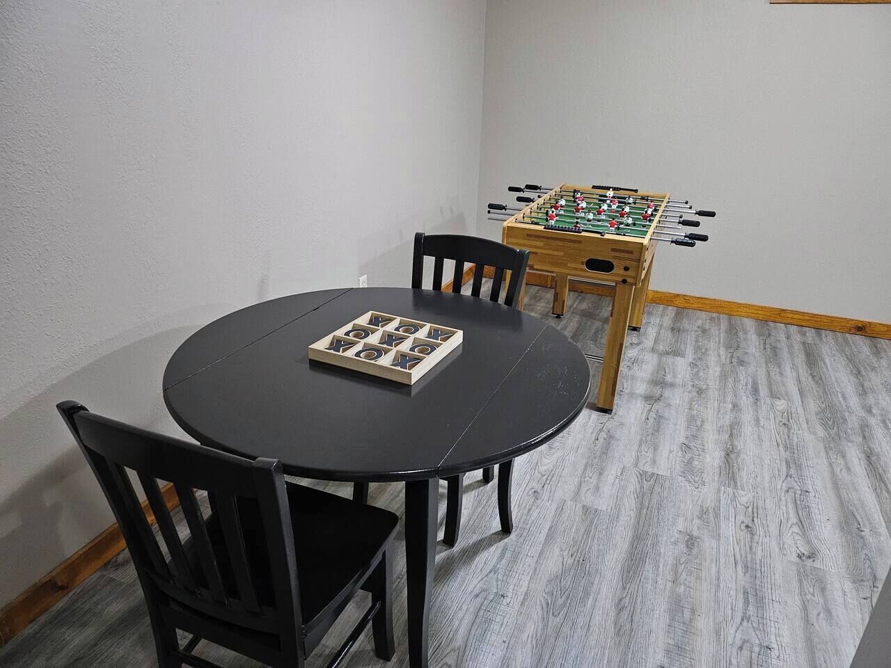 Una habitación con una mesa redonda y dos sillas, una mesa de fútbol de mesa y un tablero de juego con fichas de letras.