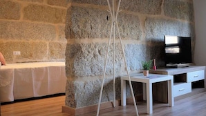 A modern living room with a stone wall, a TV, a white desk, and a sofa. - Belvilla by OYO Villa Trabazos Abellas (Ourense)