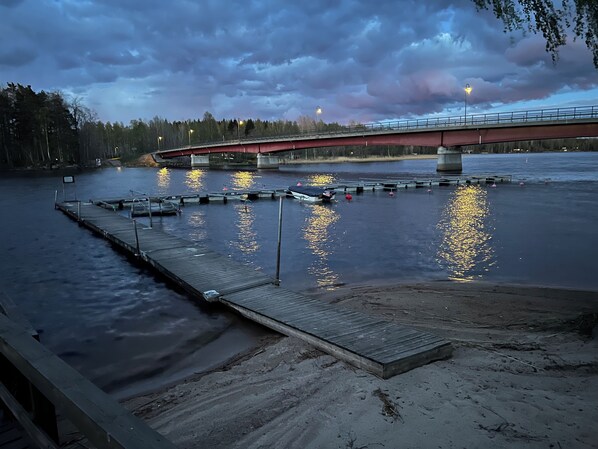 A river with a wooden dock and a red bridge in the background. - Lungsunds hotell & camping (Storfors)