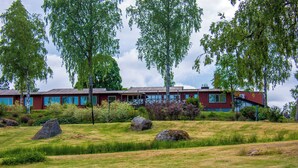 A modern building with a red facade, surrounded by a grassy area with large rocks and trees. - Lungsunds hotell & camping (Storfors)
